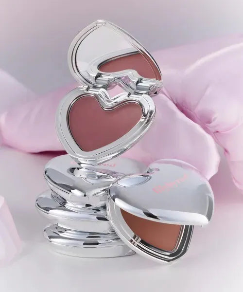 Silver heart-shaped compact mirror with pink and beige shades on a soft pink background