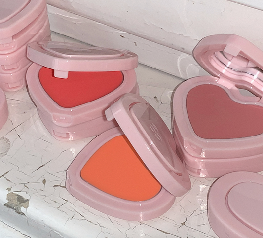 Compact blushes with pink cases on a textured white surface
