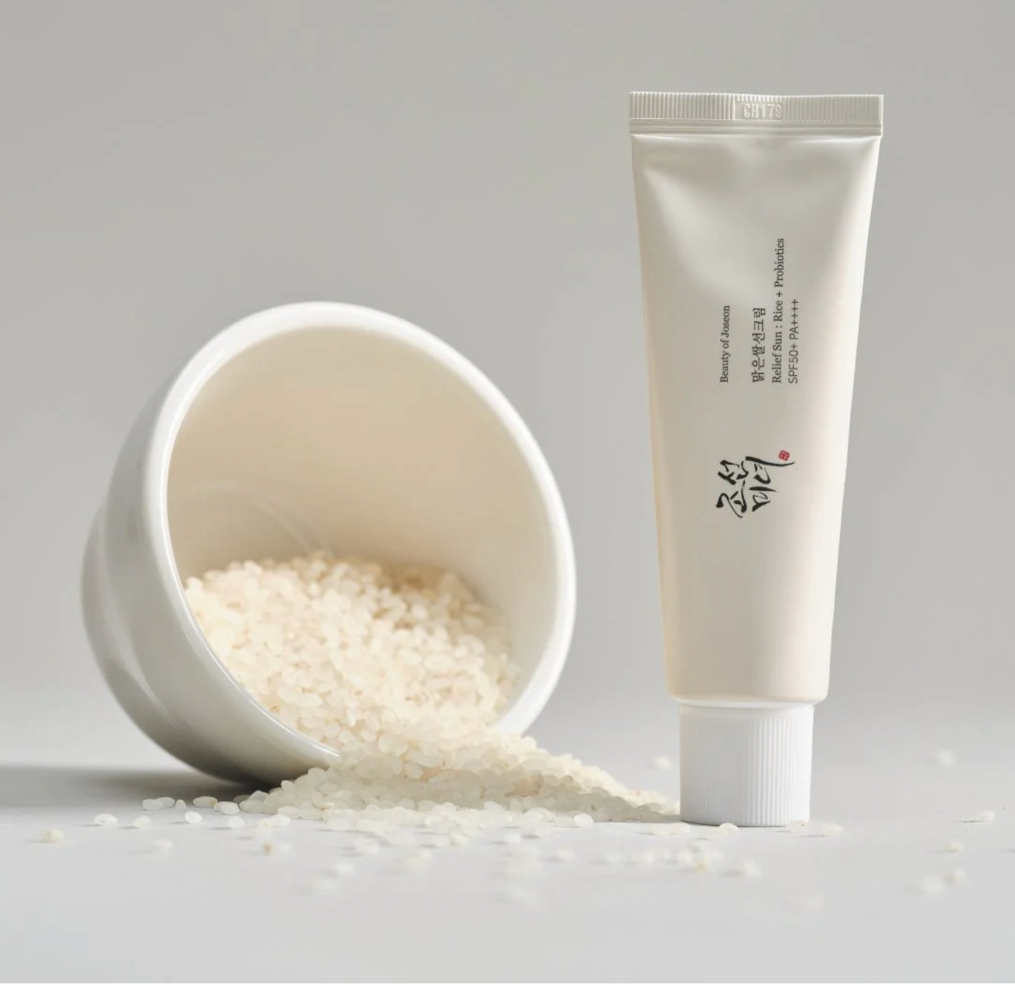 Tube of cream next to a bowl filled with white granules on a light gray background