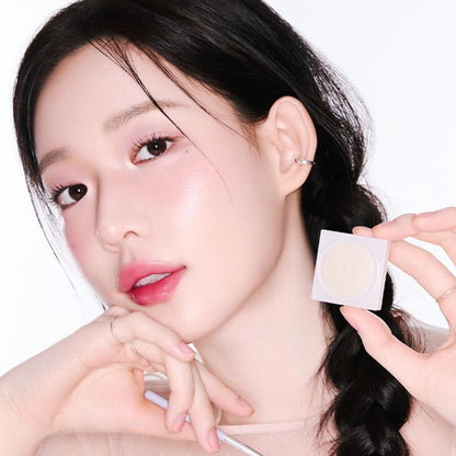 Woman holding a white square with a beige patch on a plain background. Holika Holika Luminous Milk Beam Pot for glowing Korean makeup, available at LKR