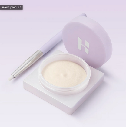 Cosmetic product with a brush on a light purple background. Holika Holika Luminous Ivory Milk Beam Pot for glowing Korean makeup, available at LKR